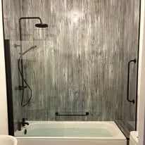 Bath with a glass screen, black rainfall shower and grey wall panels